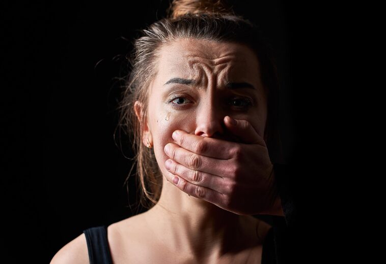 Stressed unhappy scared crying woman victim in fear with closed mouth on a dark black background suffering from female domestic violence